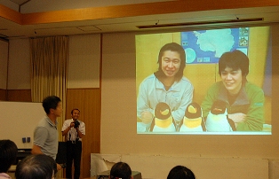 講演した伊村准教授（左）と交信する熊谷隊員（スクリーン右）