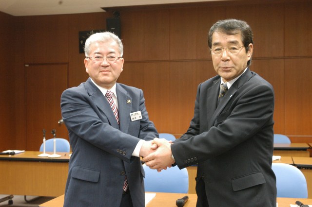 合併協議会設置の協定書に署名後、握手を交わす勝部市長（左）と畠山町長