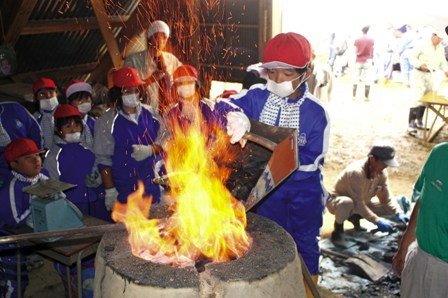 炎が燃えさかる溶鉱炉に砂鉄と木炭を入れる児童