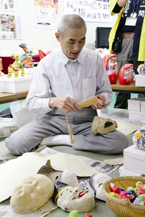 3.　三春人形に囲まれながら、重ね、湿らせた東山和紙を張り付けていく橋本広司さん