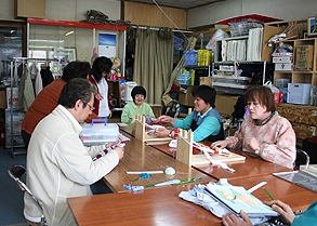 ボランティアから寄付された端切れ布で丹念に布草履を編む工房利用者。草履はオリジナル商品として販売されます