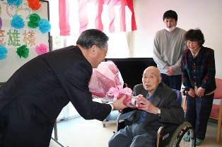 誕生祝いの品を贈られ祝福を受けた伊藤茂雄さん（中央）