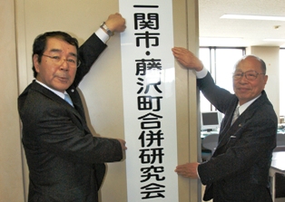合併研究会を設置し事務局の看板を掲げる浅井市長（右）と畠山藤沢町長