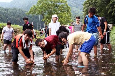 特製の古縄たわしを使い砂鉄川の石を磨く参加者たち