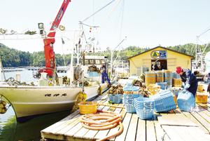 養殖いかだから船に水揚げしたカキを、加工場の前につり下ろす